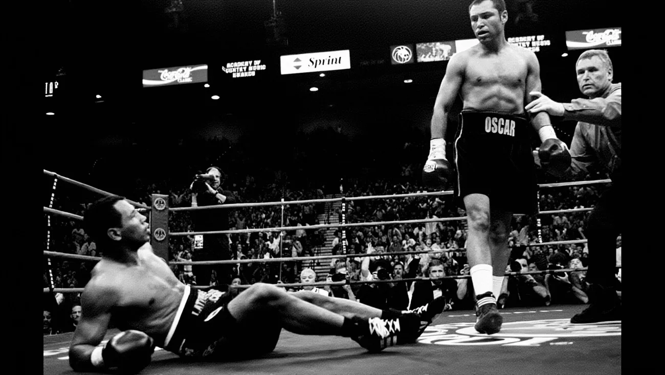Bokser stoi nad leżącym przeciwnikiem na ringu. W tle tłum widzów i tablice z reklamami, w tym Sprint i Academy of Country Music Awards. Jeden z bokserów ma szorty z napisem "OSCAR".