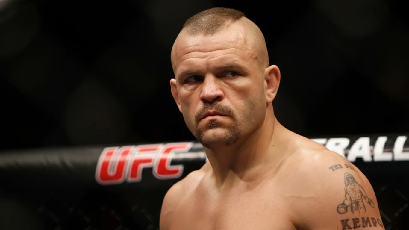 Chuck Liddell z wyrazem skupienia stoi w oktagonie. Ma wygoloną fryzurę i brodę. W tle widoczna jest bariera z napisem "UFC".