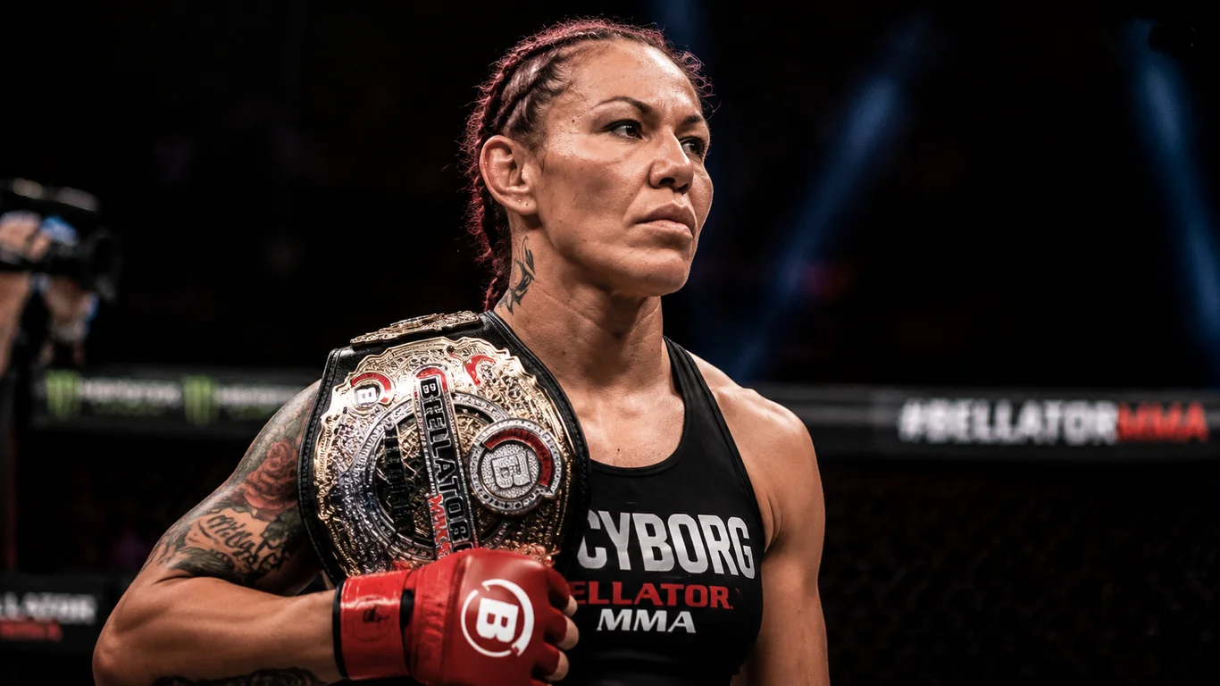 Cris Cyborg w pasie mistrzowskim Bellator MMA Featherweight w trakcie ceremonii ważenia, charakterystyczny intensywny wyraz twarzy i muskularna sylwetka.