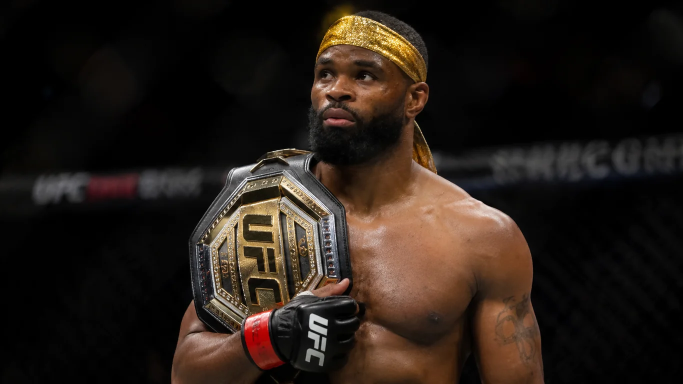 Tyron Woodley w oktagonie UFC z pasem mistrzowskim wagi półśredniej na ramieniu, charakterystyczna złota chusta na głowie i muskularna sylwetka po walce.