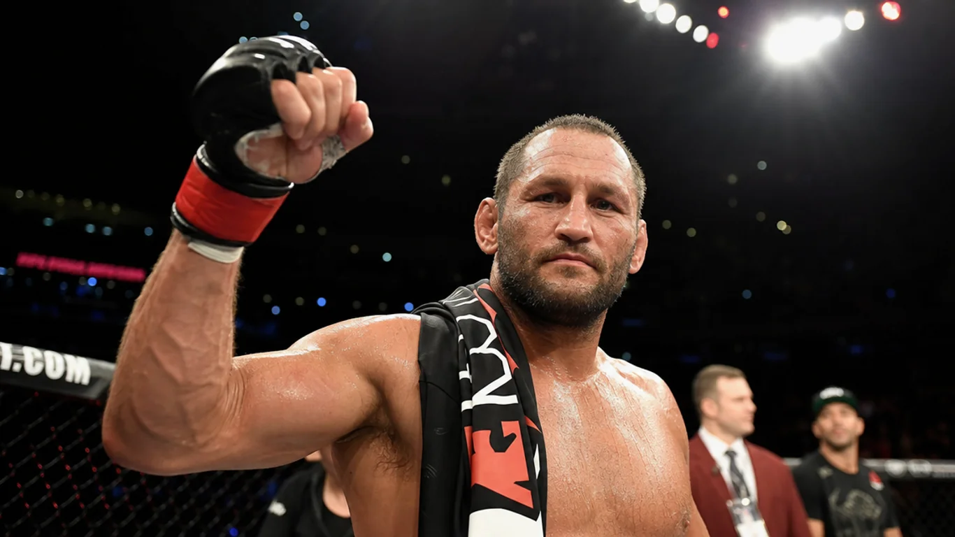 Dan Henderson Hendo w pasie mistrzowskim PRIDE FC po wygranej walce, charakterystyczne intensywne spojrzenie amerykańskiego weterana MMA z brodą, oświetlenie sceniczne japońskiej areny.