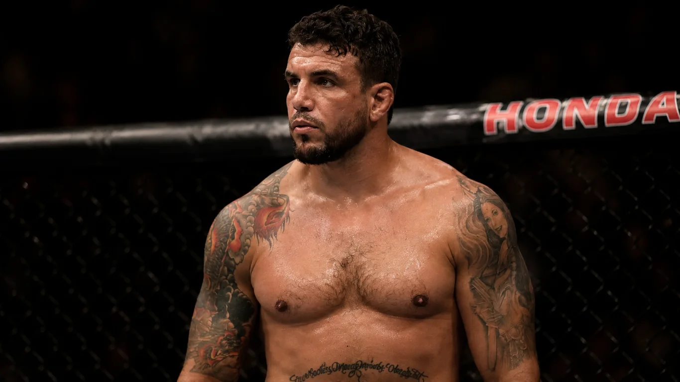 Frank Mir w pasie mistrzowskim UFC wagi ciężkiej po wygranej walce, charakterystyczna twarda twarz amerykańskiego zawodnika z brodą i tatuażami, oktagonowe oświetlenie areny.