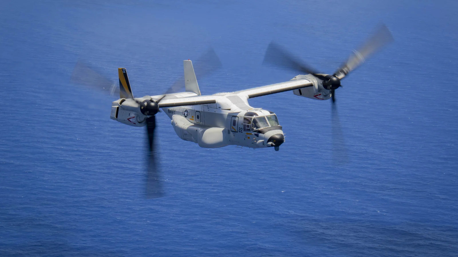 Biały CMV-22B Osprey marynarki wojennej USA w locie nad oceanem, gondole wirników w pozycji pośredniej, numer 22 na stateczniku