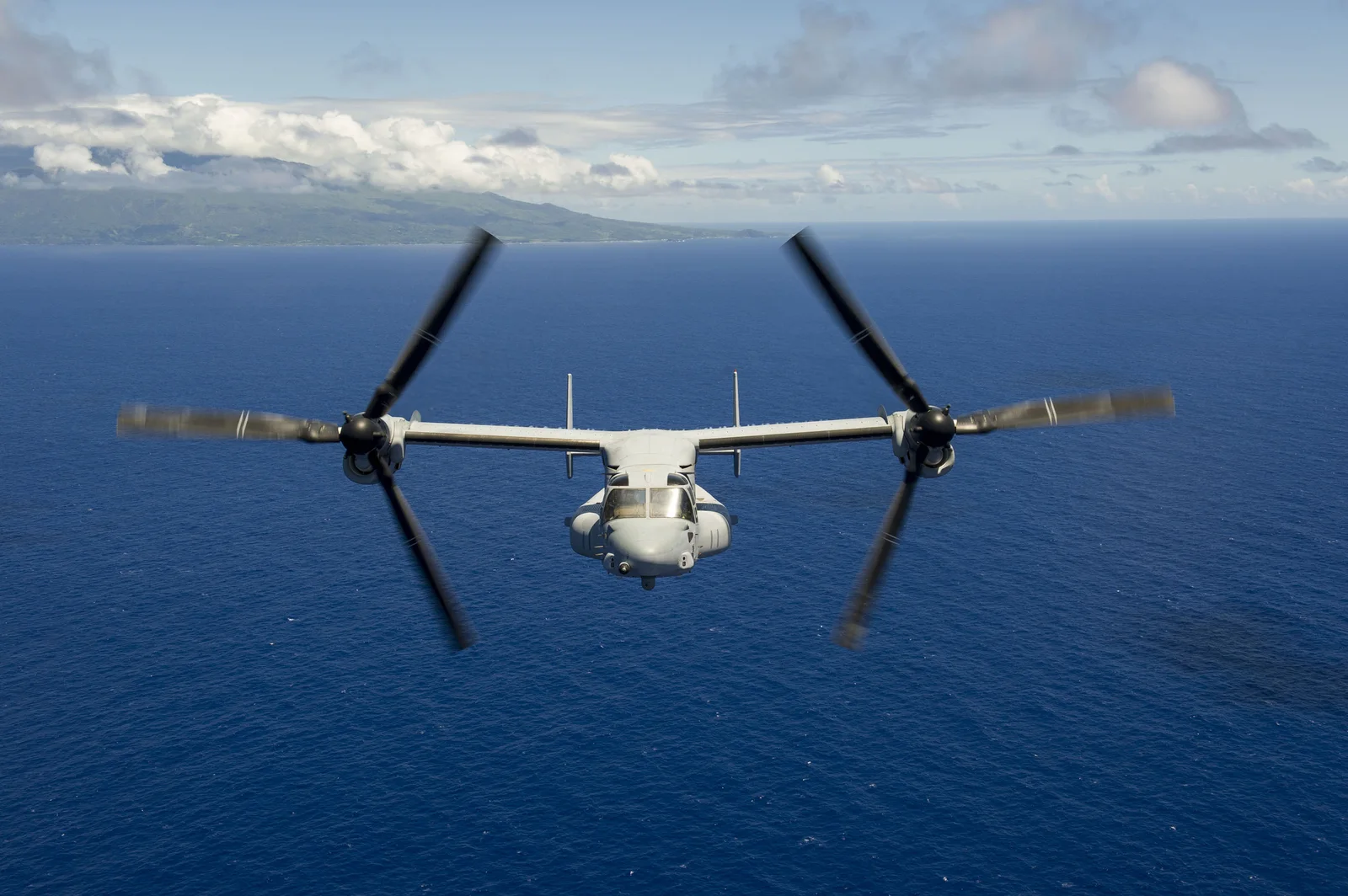 MV-22 Osprey piechoty morskiej USA lecący wprost na kamerę nad oceanem, wirniki obrócone w pozycję śmigłowcową, w tle wyspa
