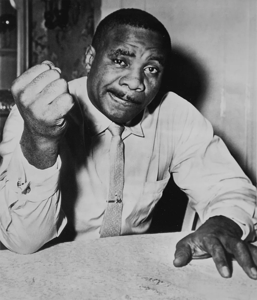 Sonny Liston w koszuli i krawacie pokazuje zaciśniętą pięść do obiektywu