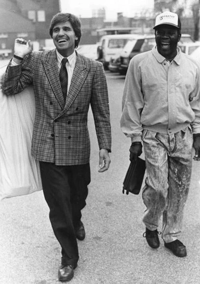 Nino Benvenuti w garniturze i Emile Griffith w kurtce i czapce z daszkiem idą razem ulicą, obaj roześmiani
