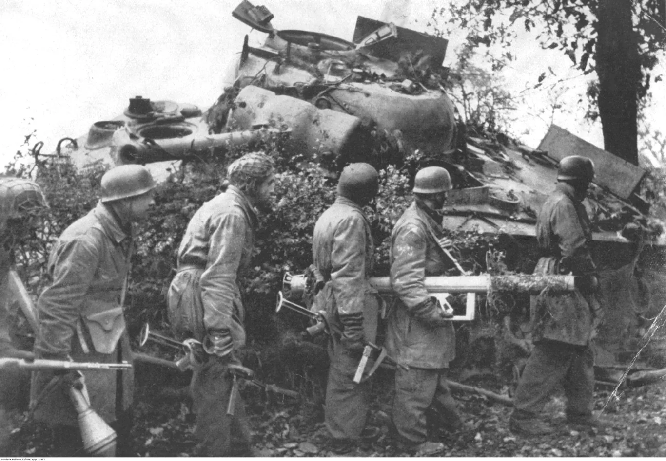 Niemieccy spadochroniarze przechodzą obok zniszczonego czołgu M4A3 Sherman z zerwaną wieżą