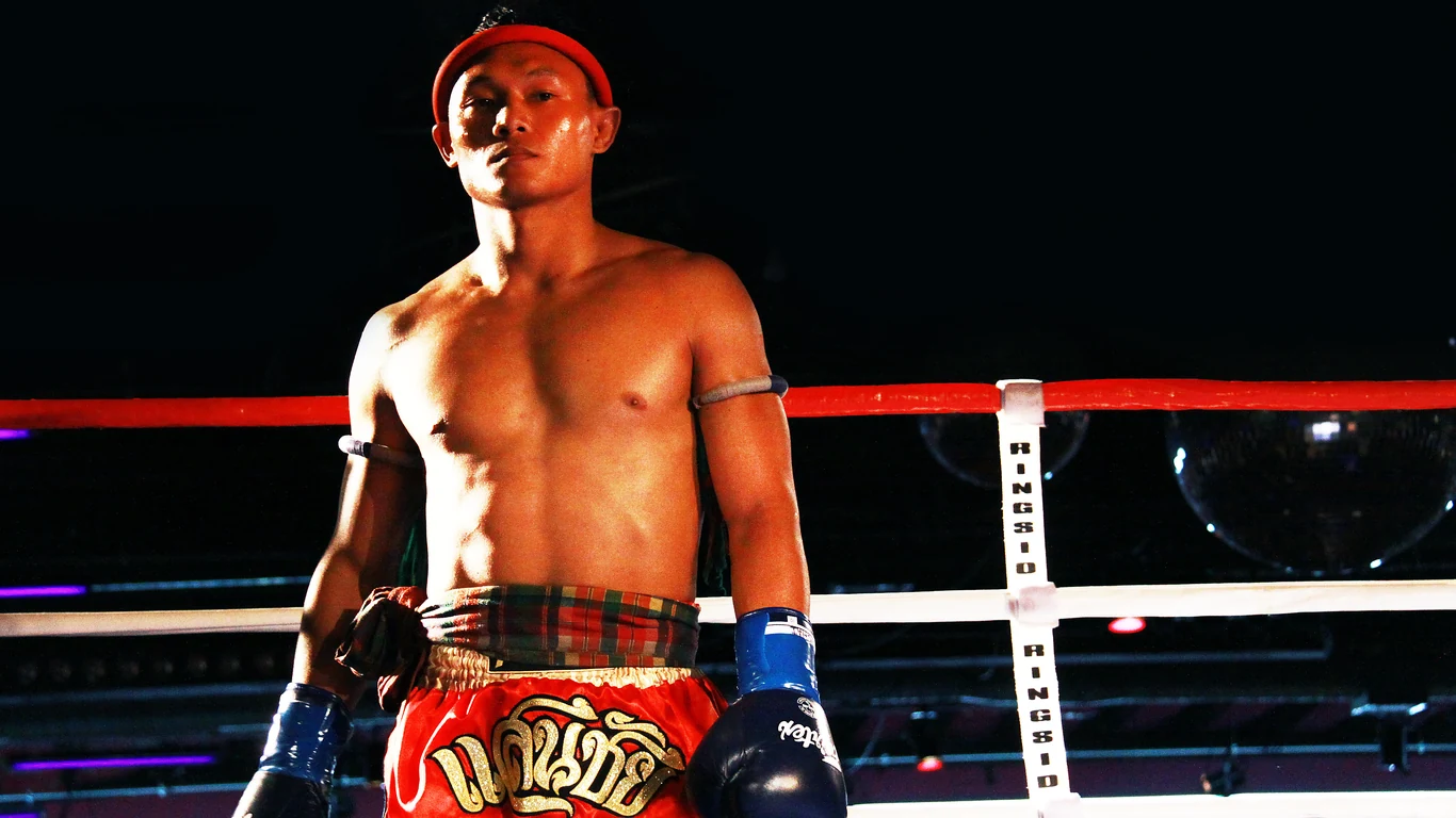 Saenchai w ringu, w opasce mongkhon na głowie i spodenkach muay thai, przed rozpoczęciem walki