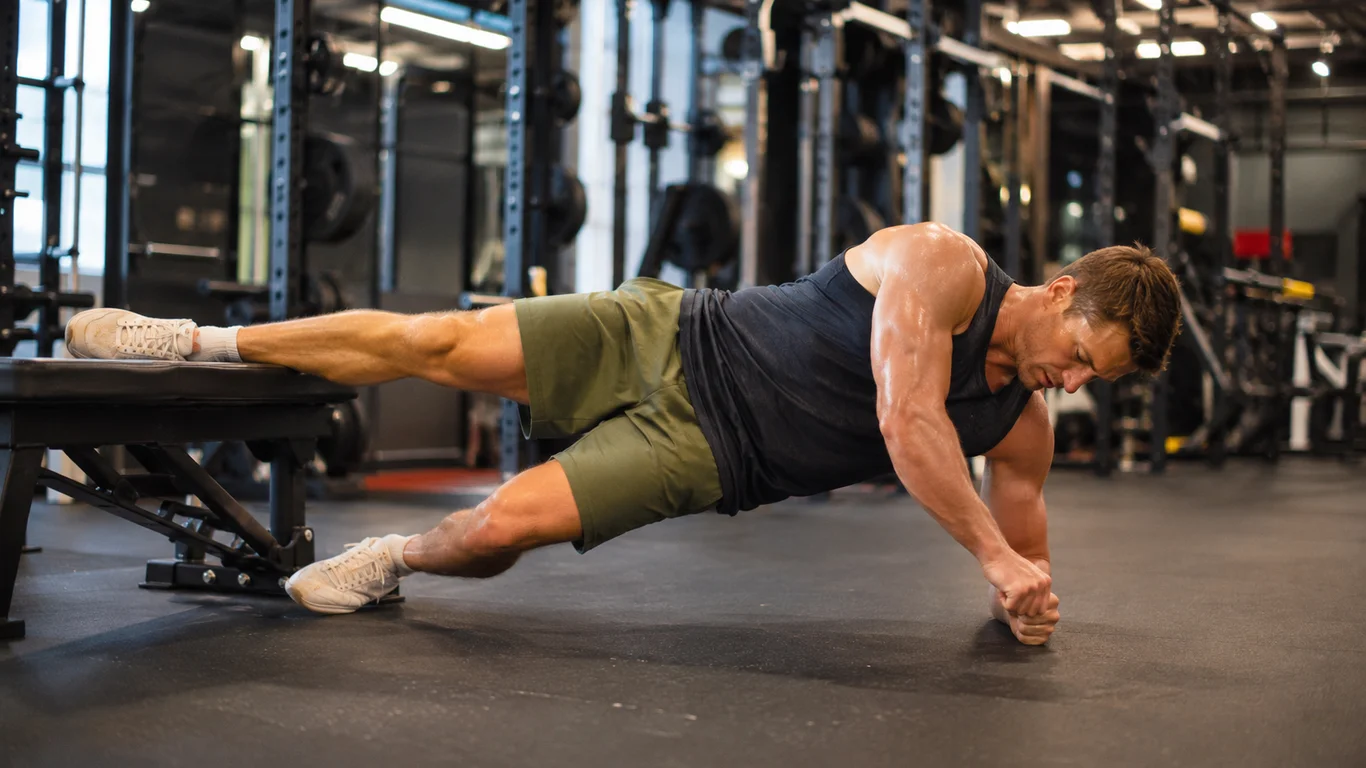 Mężczyzna w podporze bokiem na przedramieniu z górną nogą opartą na ławce i uniesionymi biodrami, wariant przywodzenia kopenhaskiego (Copenhagen plank)