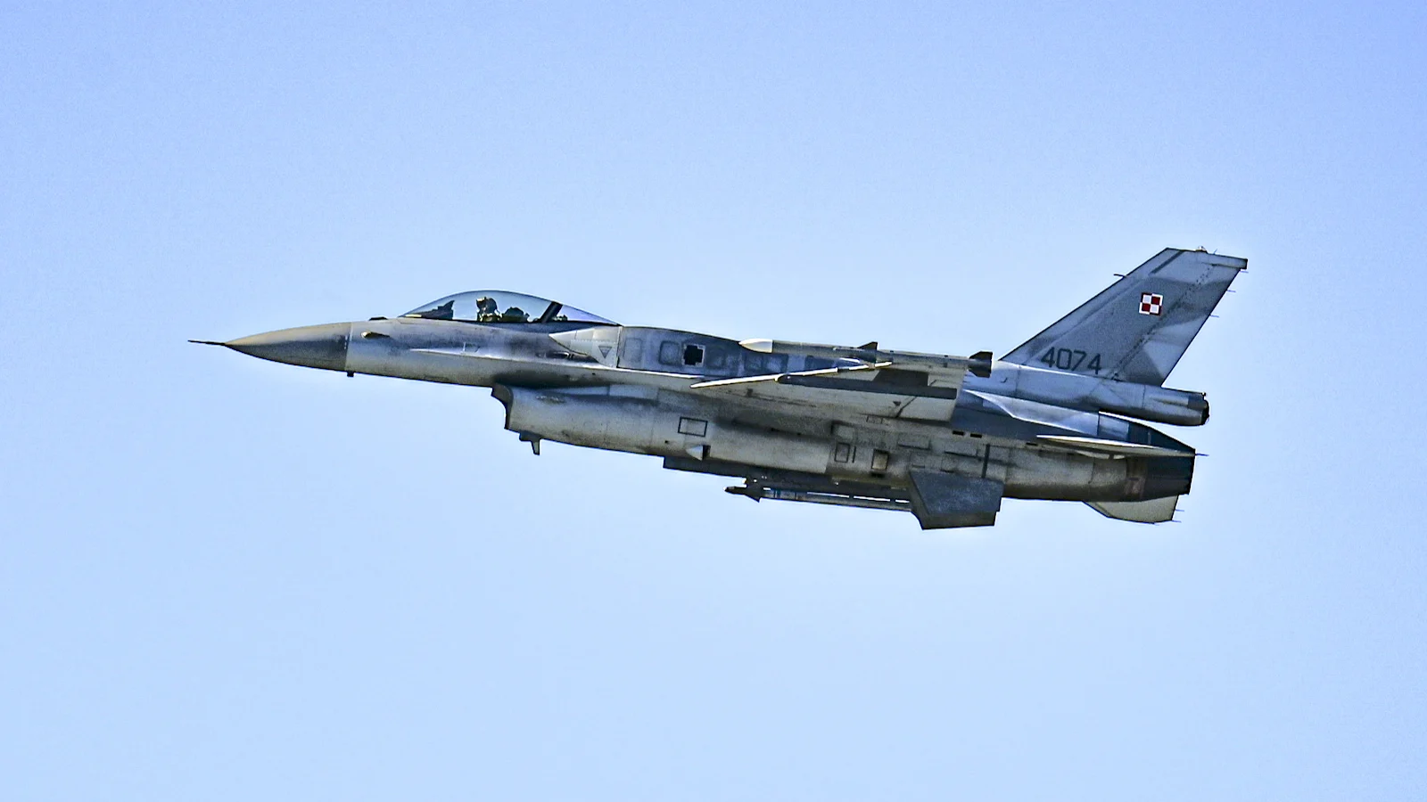 Polski myśliwiec F-16 o numerze 4074 w locie na tle czystego nieba, z biało-czerwoną szachownicą na stateczniku