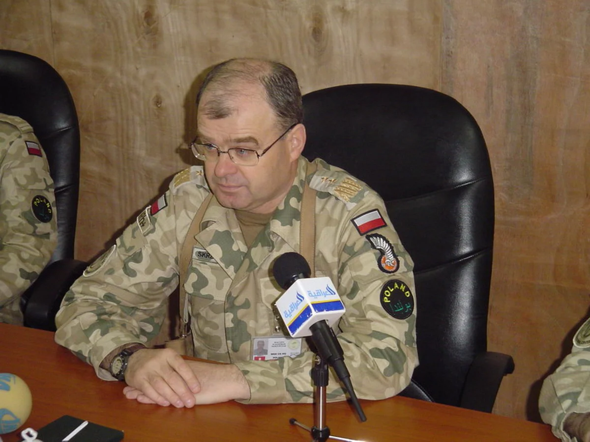 Gen. Waldemar Skrzypczak w mundurze pustynnym z naszywką POLAND i orłem 11 Dywizji Kawalerii Pancernej przemawia do mikrofonu irackiej telewizji w bazie Echo